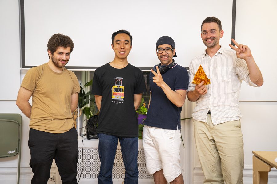 Une équipe de hackathon de quatre personnes devant l’écran, l’une tenant une pointe de pizza